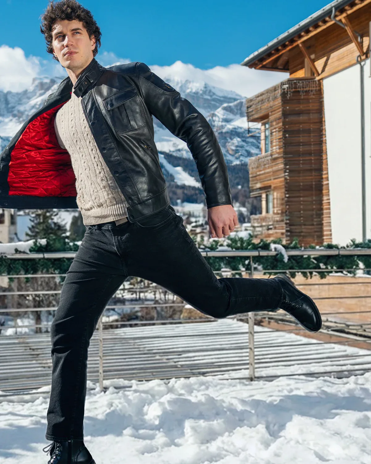 Dynamic mid-air shot in a leather jacket with red lining, snowy mountains in the background