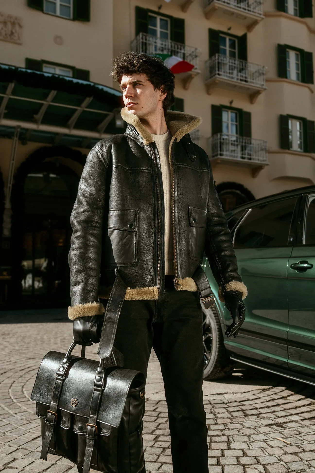 Portrait in a sheepskin jacket with a leather bag in front of a building in Cortina d'Ampezzo