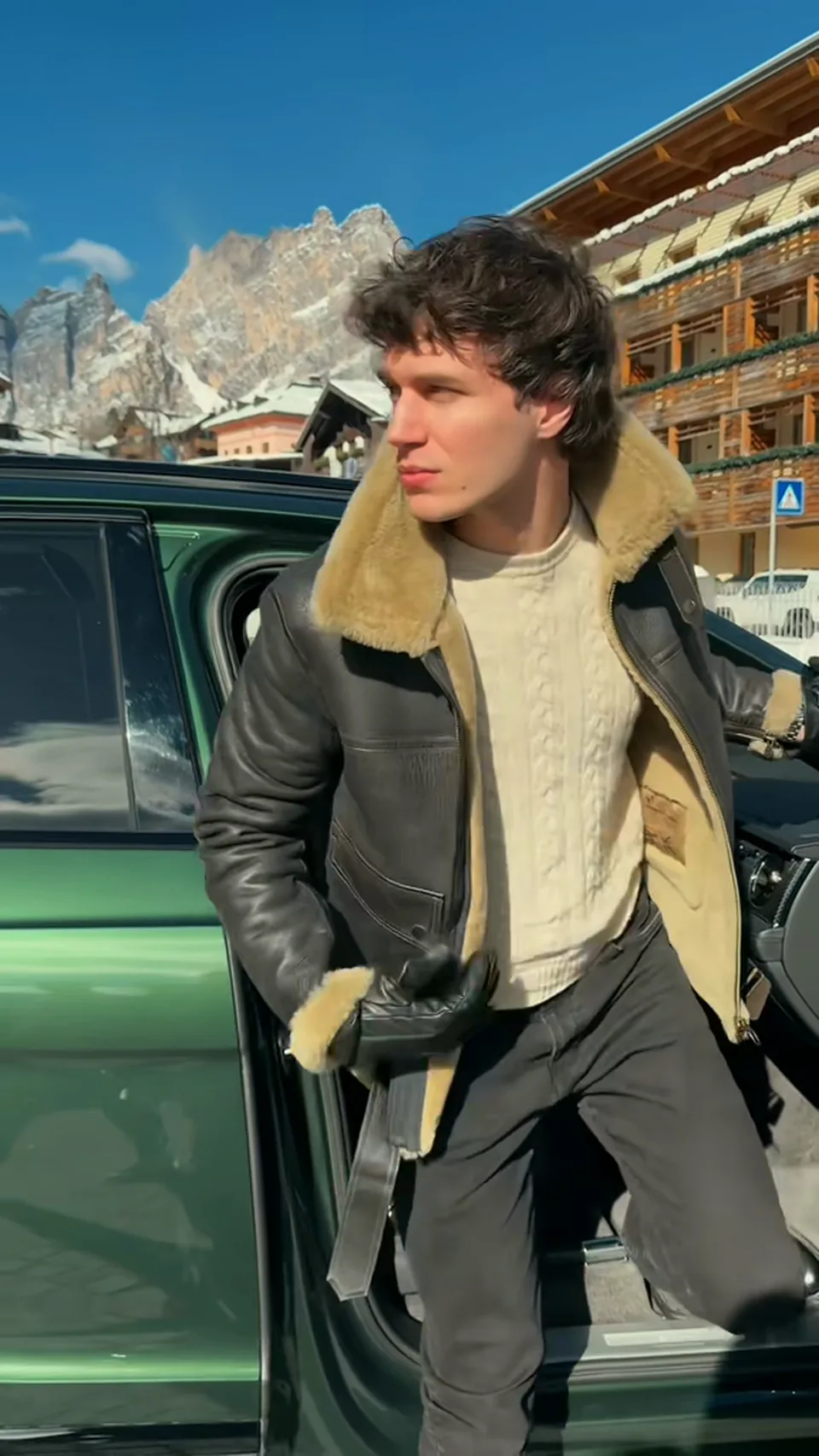 Francesco Scarparo gets out of a car in Cortina d'Ampezzo in a sheepskin jacket, with the Dolomites behind him